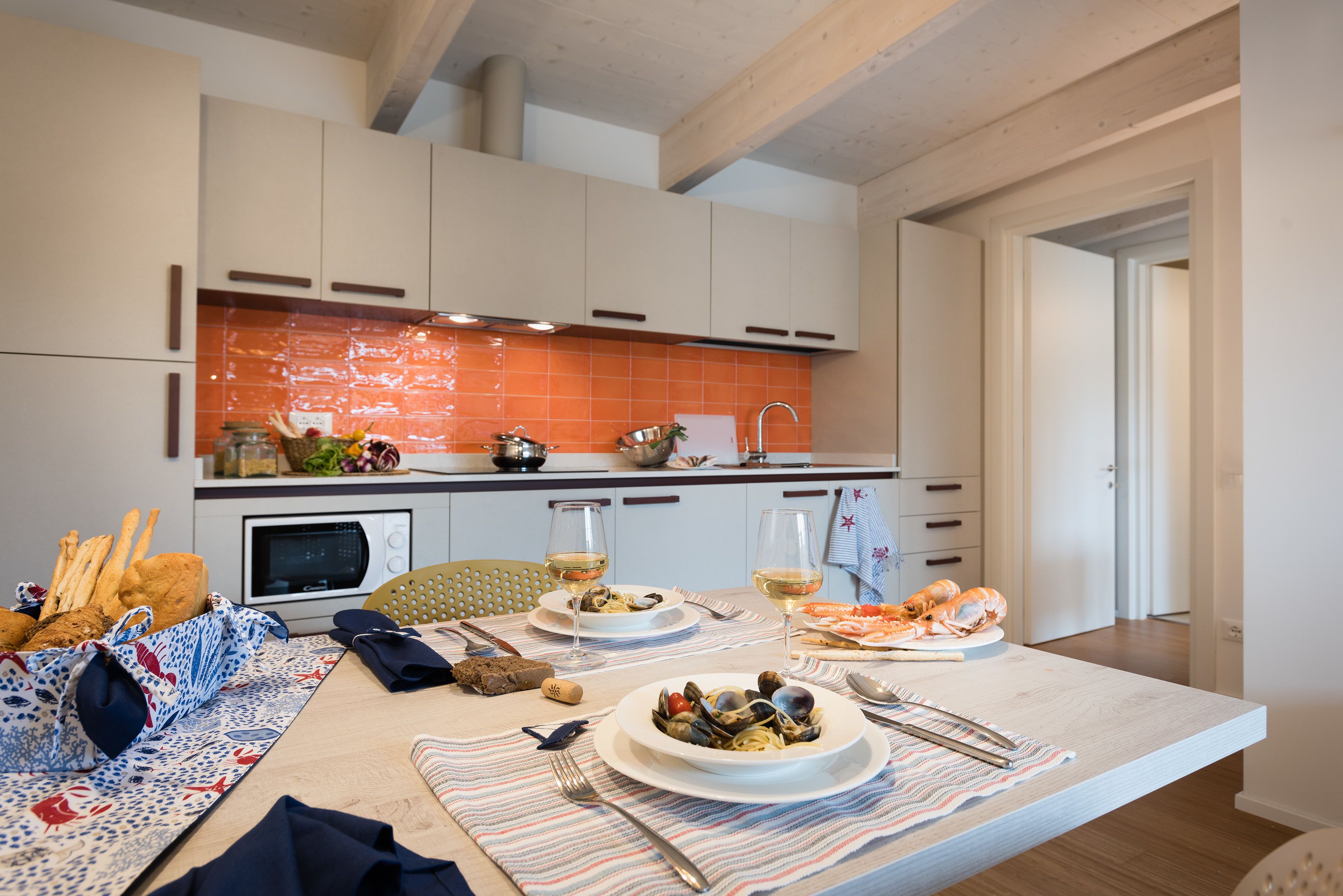 Una cocina moderna con armarios blancos, salpicadero naranja y una zona de comedor con una mesa dispuesta para una comida.