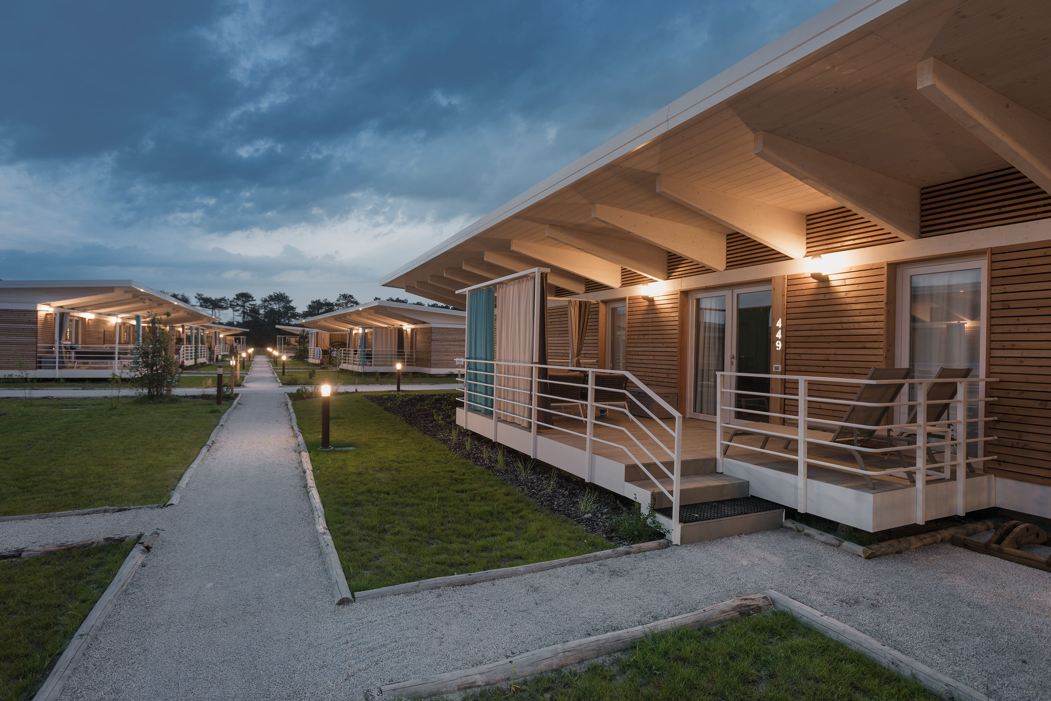 A row of modern, single-story cabins with outdoor seating areas and a gravel pathway leading through the property.