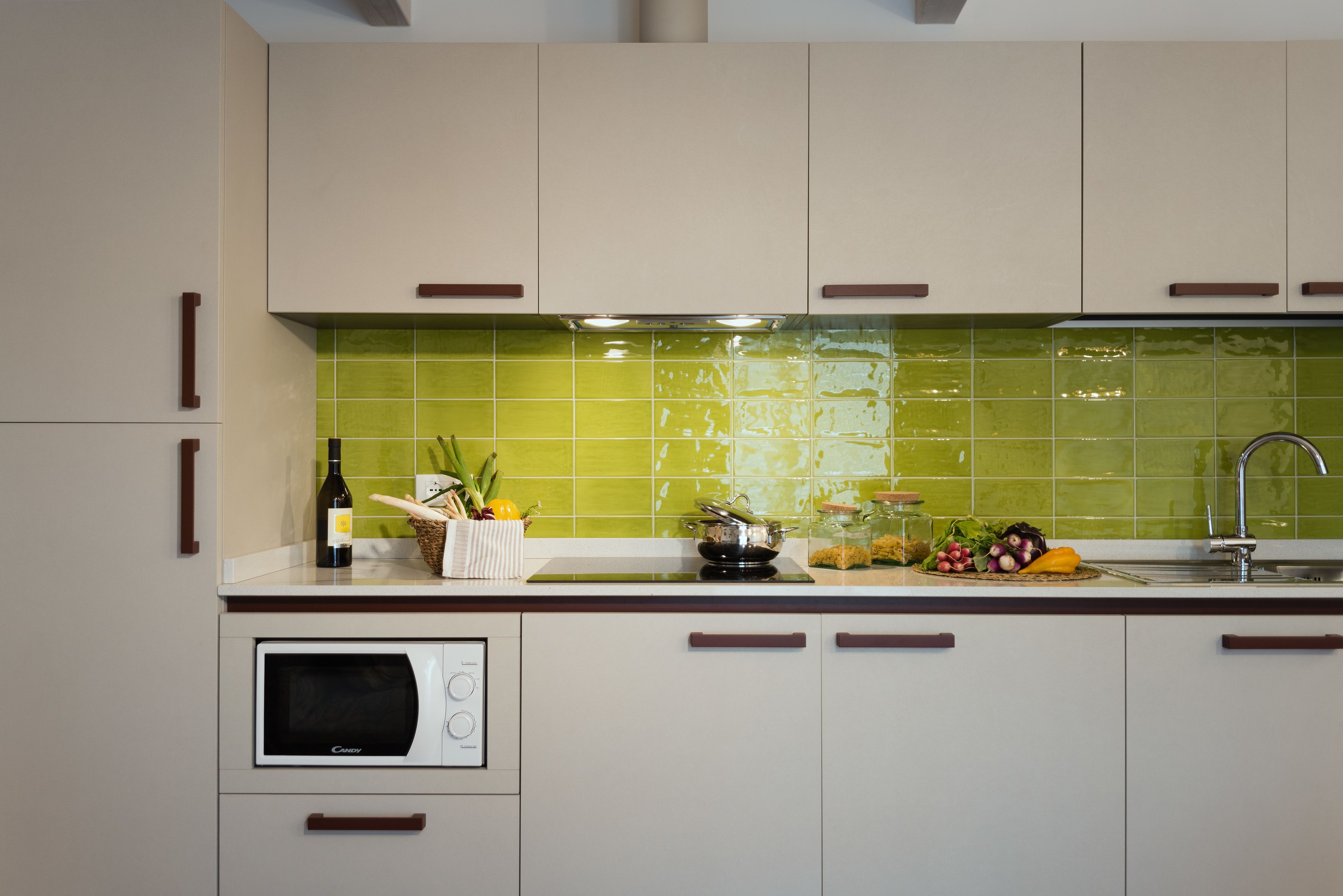 A modern kitchen with light-colored cabinets, a microwave, and a green tiled backsplash.