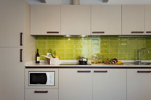 A modern kitchen with light-colored cabinets, a microwave, and a green tiled backsplash.