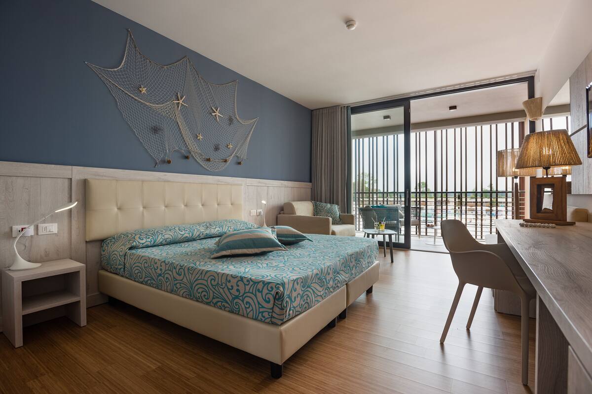 A modern hotel room with a large bed, a desk, and a balcony with a view.