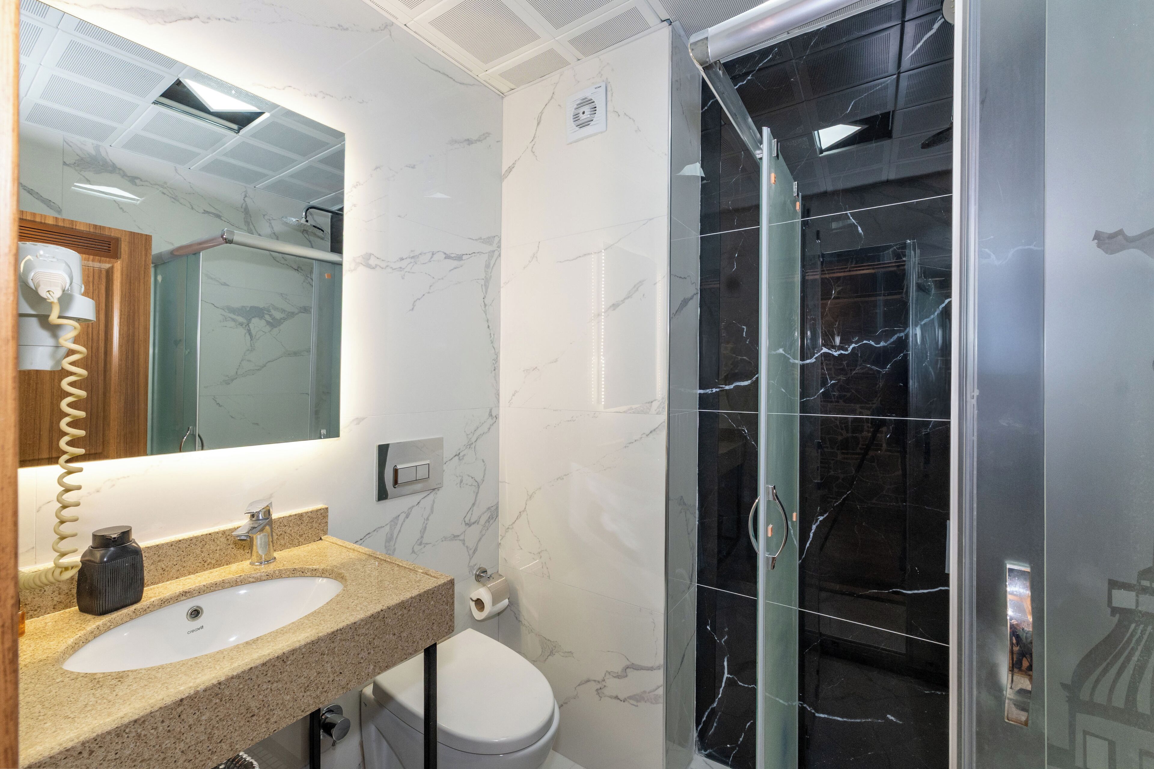 A bathroom with a marble sink, a toilet, and a glass-enclosed shower.
