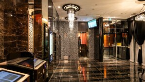 Un hall d’hôtel moderne avec un sol en marbre, un kiosque d’information numérique et un grand lustre.
