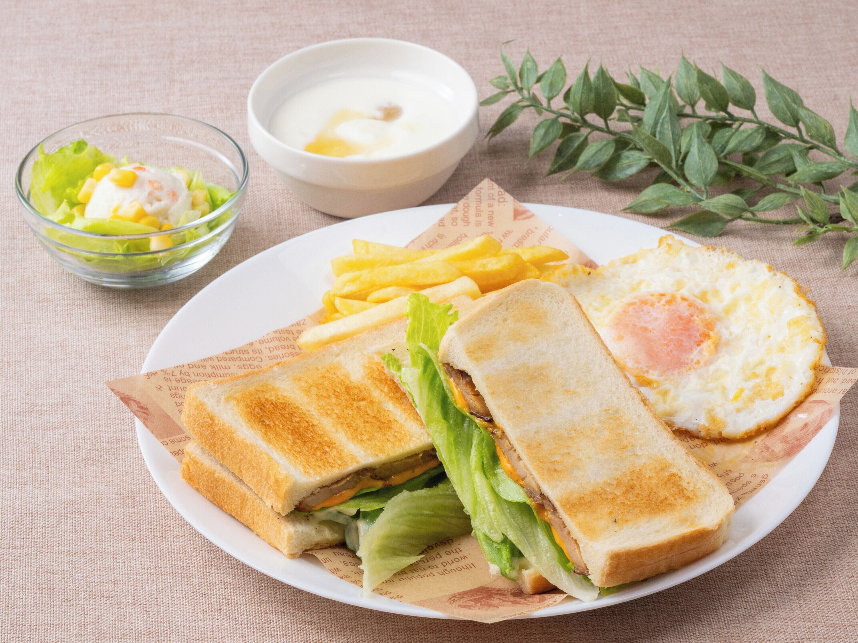 A plate with a sandwich, a fried egg, and fries, accompanied by a bowl of salad and a small bowl of sauce.