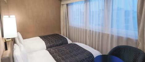 Ein Hotelzimmer mit einem Bett, zwei Kissen, einem Nachttisch, einem Sessel und einem Fenster mit Vorhängen.
