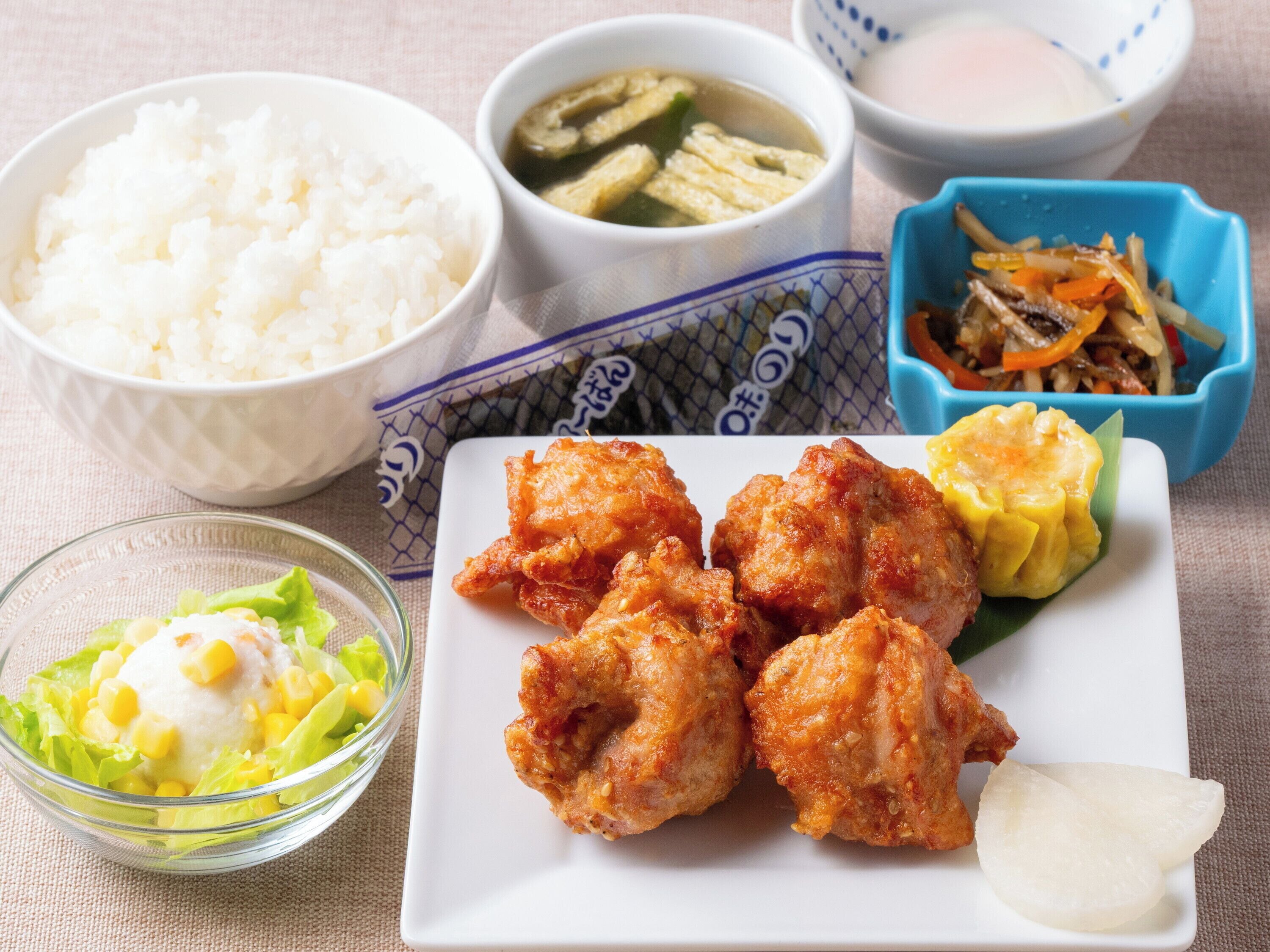 A plate of fried chicken, rice, soup, and a side salad.