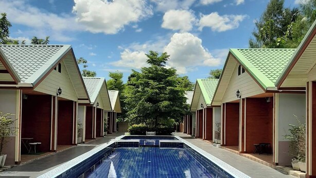 Zona de piscina bajo un cielo despejado, rodeada de edificios con techos verdes y puertas de madera.