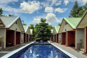 Zona de piscina bajo un cielo despejado, rodeada de edificios con techos verdes y puertas de madera.