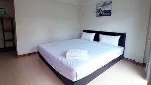 Una cama bien hecha con sábanas y almohadas blancas en una habitación con paredes blancas y suelo de madera.