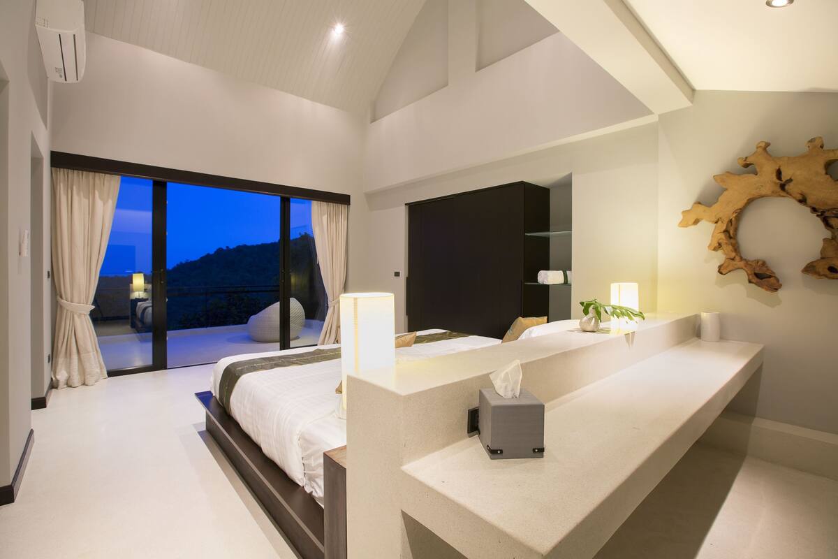 Un dormitorio moderno con una cama grande, una mesita de noche con caja de pañuelos y vistas al exterior.