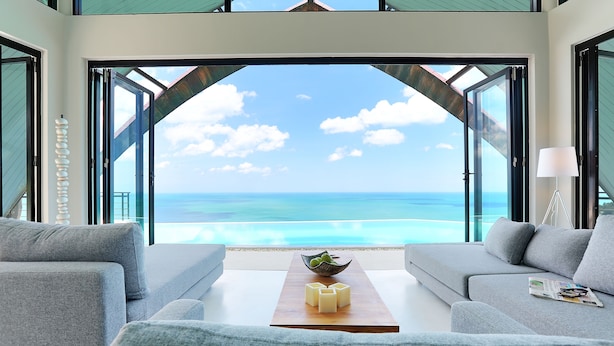 Una sala de estar moderna con un gran ventanal que da a un balcón con vistas a la playa.