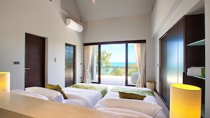 Habitación de hotel con dos camas, un ventanal amplio con vista al mar, un armario y una lámpara de noche.
