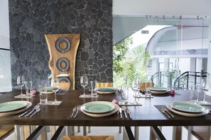 Mesa de comedor dispuesta con platos, cubiertos y vasos, con una pared de piedra y una obra de arte de madera al fondo.