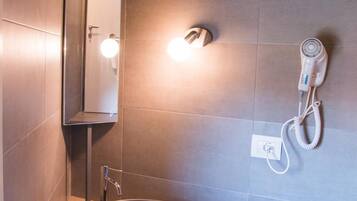 A bathroom with a wooden vanity, a vessel sink, a mirror, a hairdryer, and a towel rack.