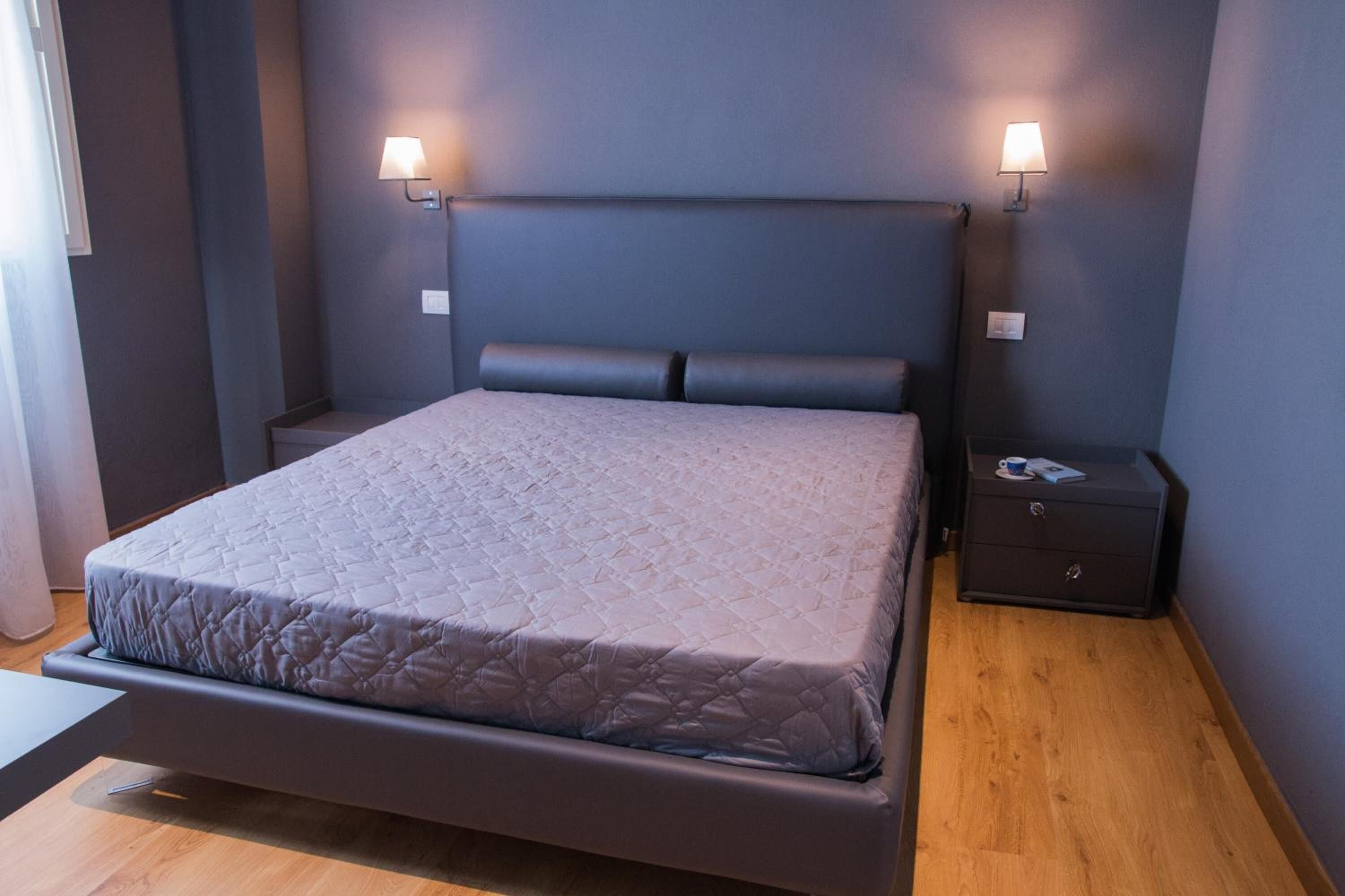 Quarto moderno com cama grande, duas mesas de cabeceira e luminárias fixadas na parede.