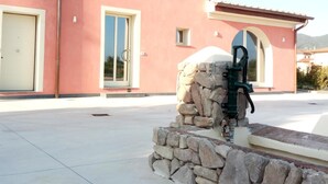A pink building with multiple windows and doors, a stone structure in front, and a clear sky. - B&B Silvia (Vecchiano)