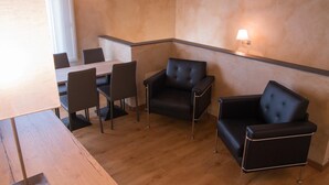 A modern room with a wooden table and chairs, two black leather sofas, and wall-mounted lamps. - B&B Silvia (Vecchiano)