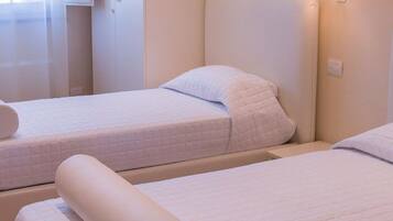 Two twin beds with white bedding and pillows, a bedside table, and a window with sheer curtains.