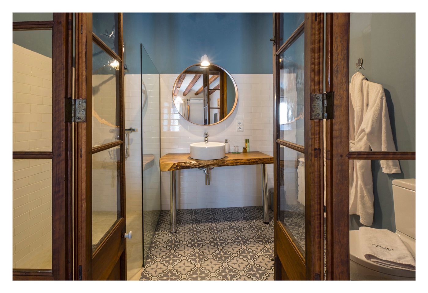 A bathroom with a wooden vanity, a round mirror, and a white sink.