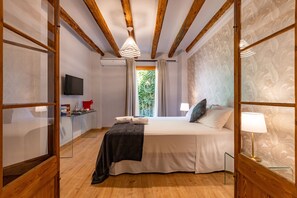 A bedroom with a wooden ceiling, a bed with a white duvet, a bedside table with a lamp, and a TV on the wall. - El Palauet del Priorat (Cornudella de Montsant)