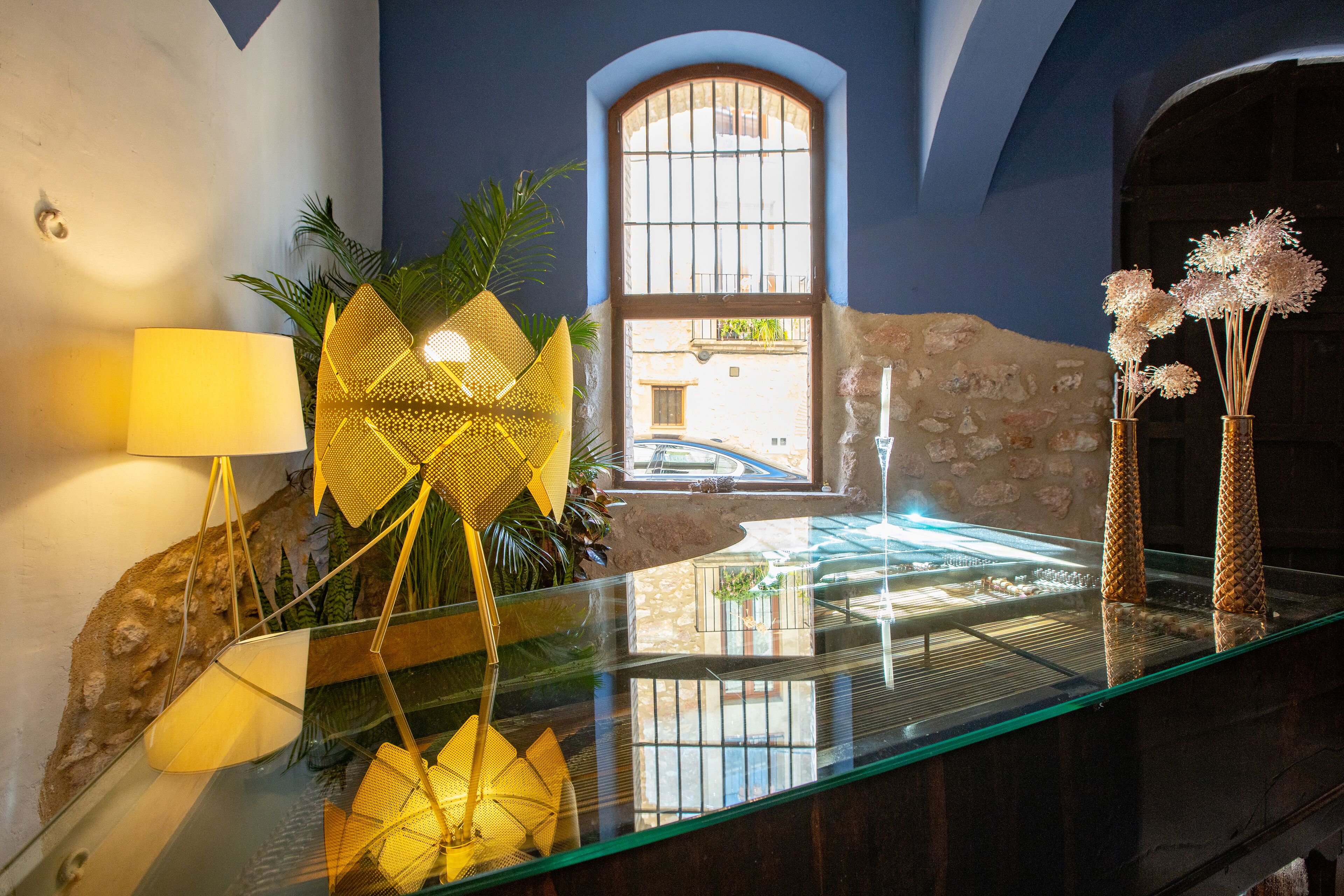 A glass table with decorative items, a lamp, and a view of a street through a window.