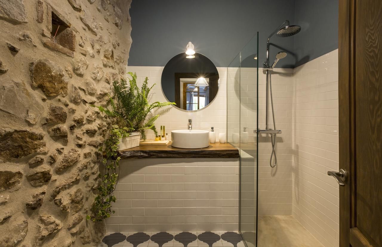 A bathroom with a stone wall, a round mirror, a sink, and a shower.