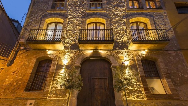 Un edificio de piedra con puerta de madera, varias ventanas y balcones con barandillas de metal.