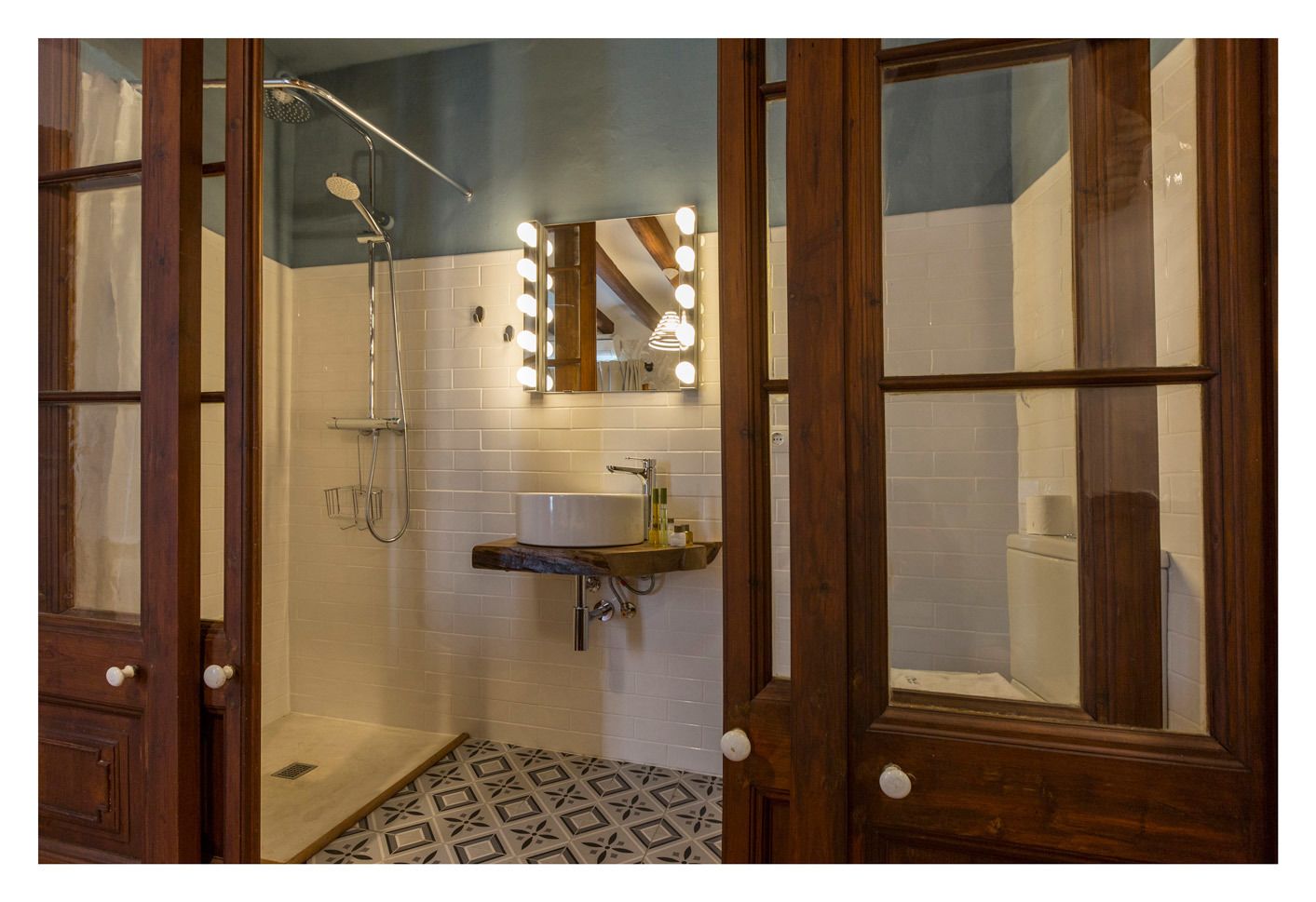 A bathroom with a shower, a sink with a mirror, and a patterned floor.