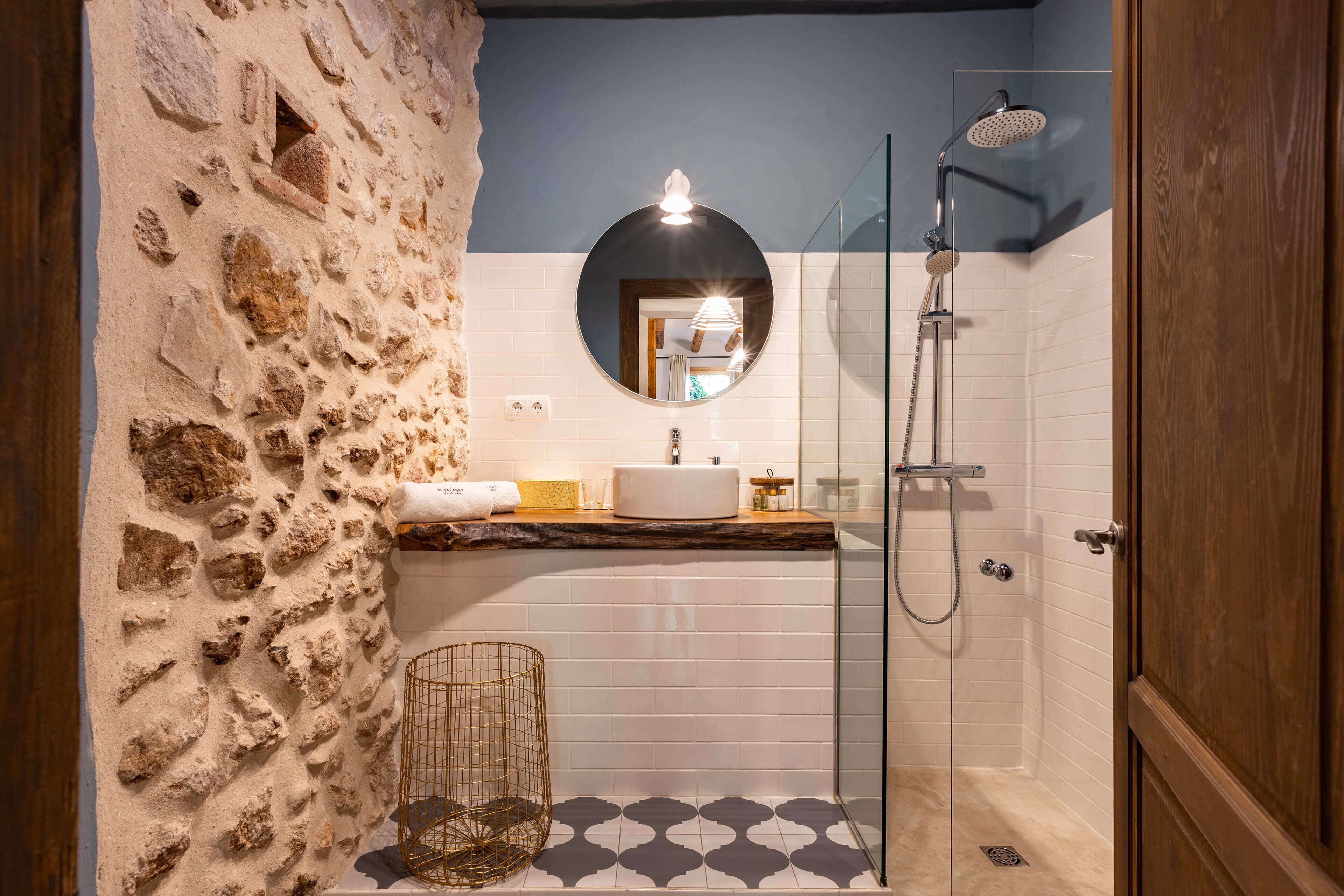 Ein Badezimmer mit Steinwand, rundem Spiegel, Waschbecken und Dusche.
