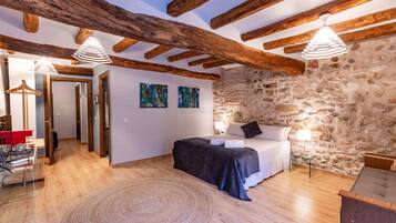 Un dormitorio con pared de piedra, vigas de madera, cama, mesita de noche y lámpara colgante.