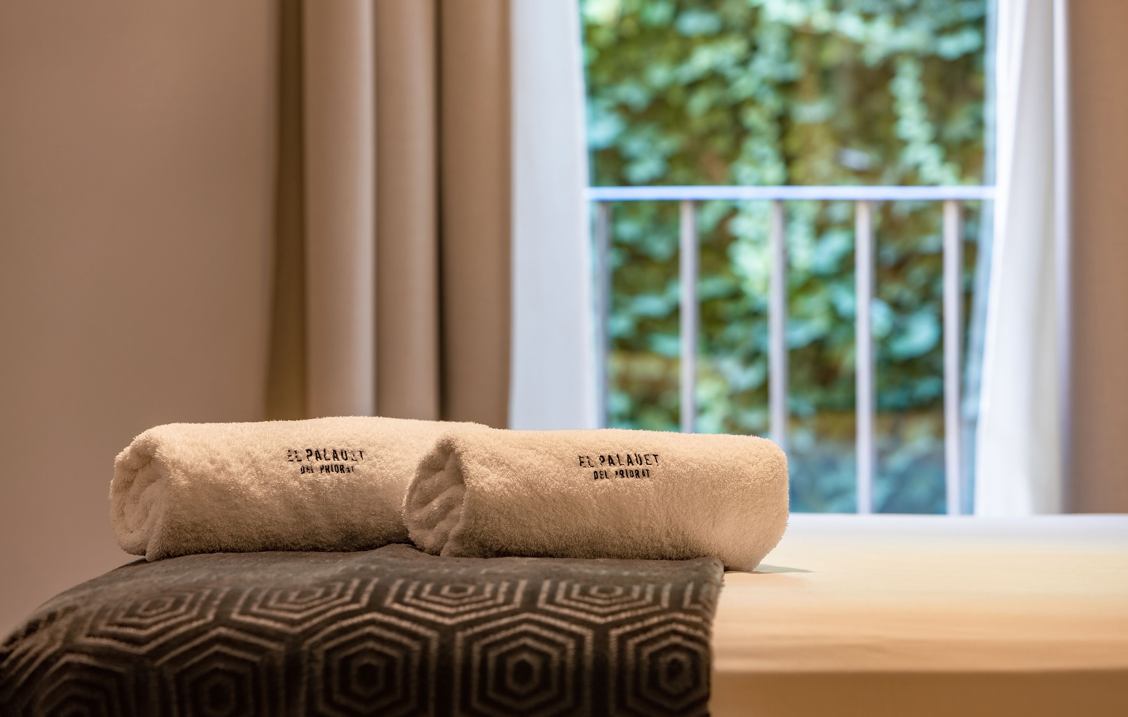 Una cama bien hecha con dos toallas enrolladas y una almohada estampada.