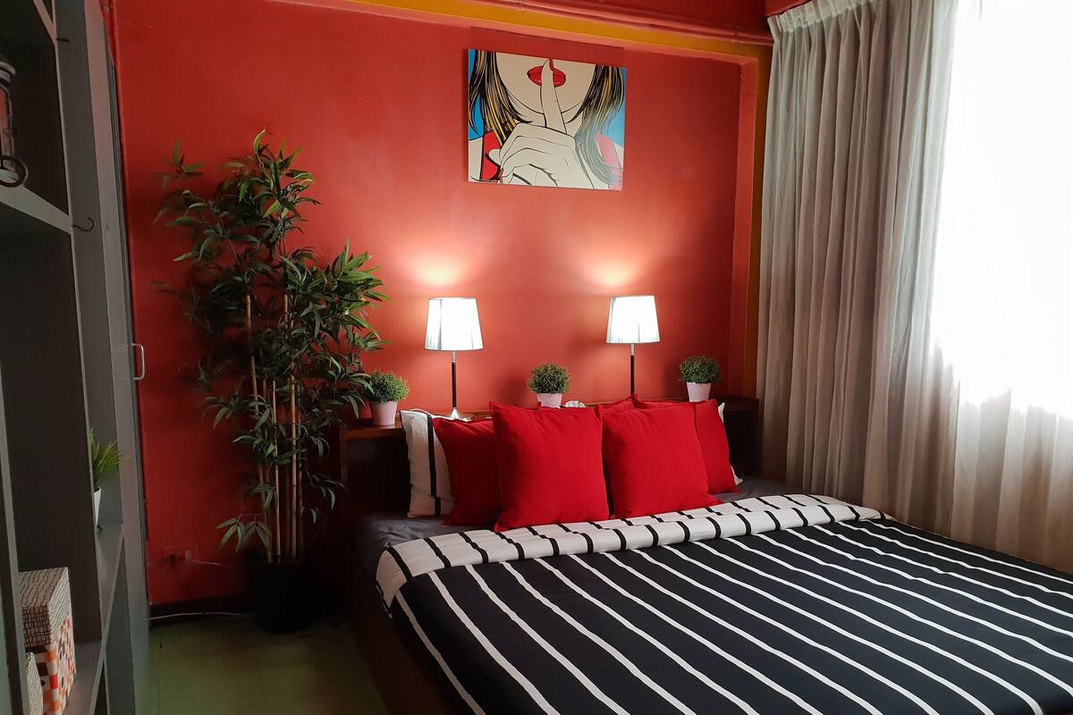 Ein Hotelzimmer mit roter Wand, einem Bett mit schwarz-weiß gestreifter Bettwäsche, zwei Nachttischlampen und einem Gemälde über dem Bett.