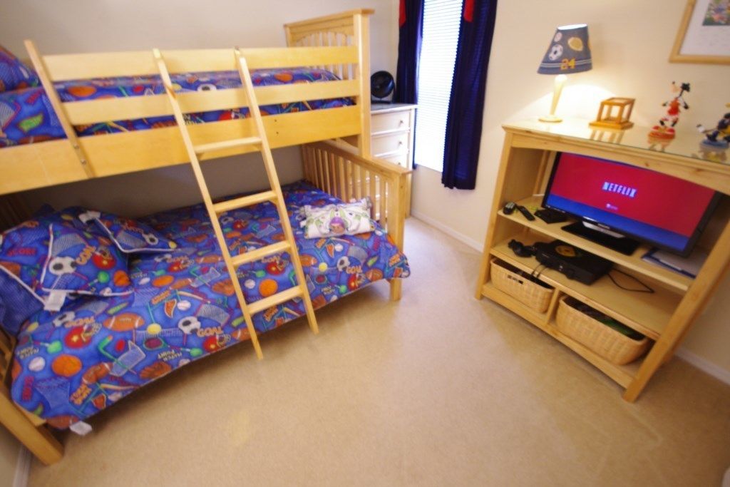 A bunk bed with a ladder, a desk with a computer, a TV, and a shelf with storage baskets.