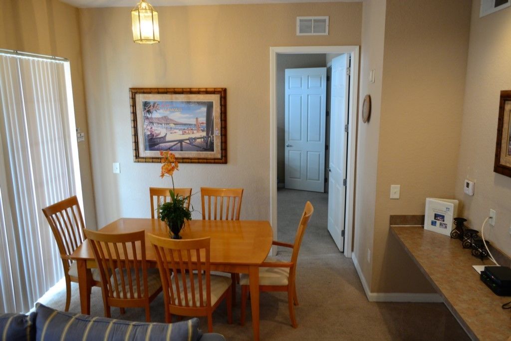 A dining area with a wooden table and chairs, a framed picture on the wall, and a door leading to another room.