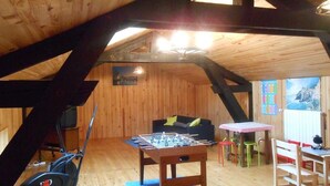 Een kamer op zolder met een tafelvoetbaltafel, een hometrainer en een gezellige zithoek met een bank en stoelen.