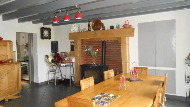Een eethoek met een houten tafel, stoelen en een kroonluchter. Er is een open haard en een klok aan de muur.