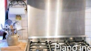 Een keuken met een roestvrijstalen fornuis, een decoratief kunstwerk erboven en een houten snijplank met keukengerei.