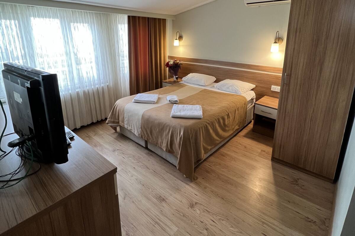 A hotel room with a bed, bedside tables, a desk with a computer, and a window with curtains.