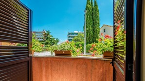 Un balcon donnant sur un jardin, un grand arbre et des bâtiments en arrière-plan.