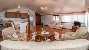 Un vaste espace de vie doté d’un plancher en bois, d’une table à manger avec des chaises, d’un canapé, d’un téléviseur et d’un lustre.