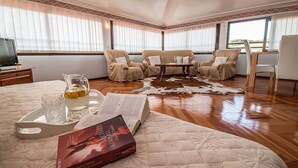 Une pièce chaleureuse avec un lit, un coin lecture agrémenté d’un livre et d’une boisson, un tapis en peau de vache et une vue dégagée grâce à de grandes fenêtres.