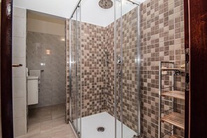 A modern bathroom with a glass-enclosed shower, tiled walls, and a wooden shelf unit. - Villa Rose (Rovinj)