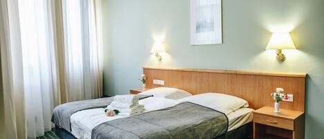 A hotel room with a bed, two bedside tables, a nightstand, a lamp, a framed picture on the wall, and a window with curtains.