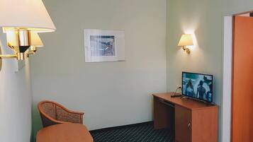 A hotel room with a single bed, a desk with a television, and two wall-mounted lamps.