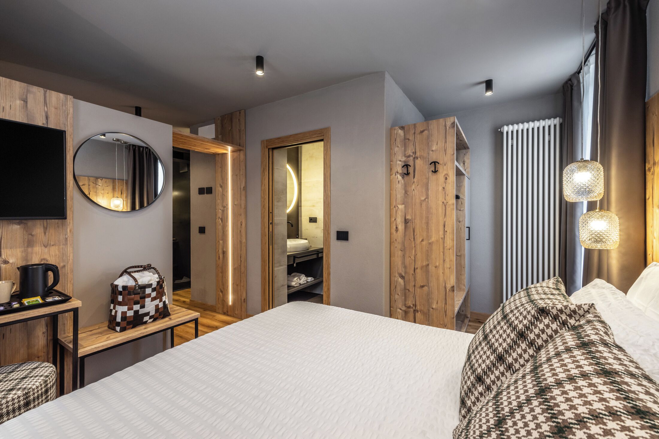 A modern hotel room with a bed, a desk with a coffee maker, a mirror, and a wardrobe.