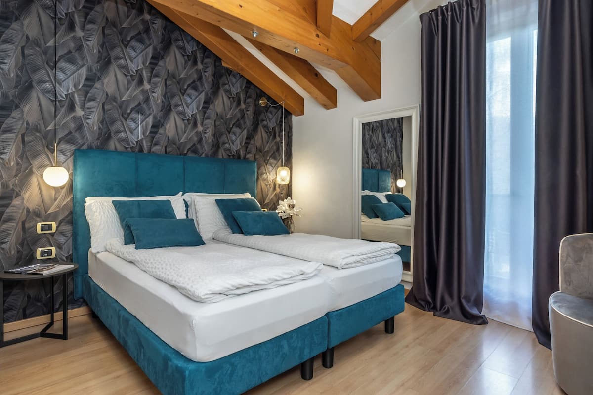 Ein modernes Schlafzimmer mit einem großen Bett, Holzbalken, einem Spiegel und Blick ins Freie.