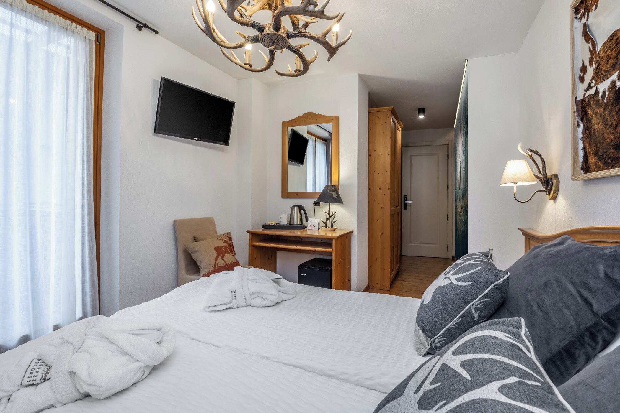 Habitación de hotel con cama, escritorio, silla, televisión, espejo, candelabro y lámpara de pared.