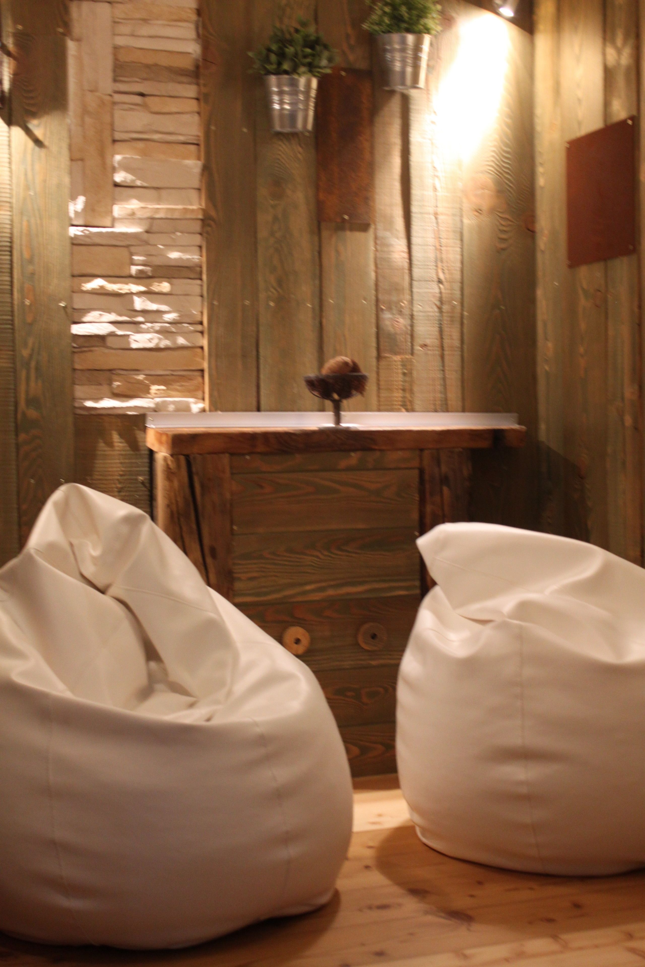 A rustic wooden interior with a stone wall, a wooden table with a plant, and two white bean bags.
