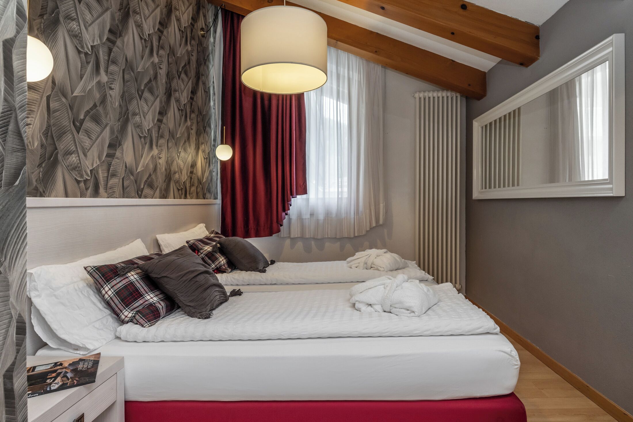 Un dormitorio con dos camas, techo de madera, radiador y ventana con cortinas.