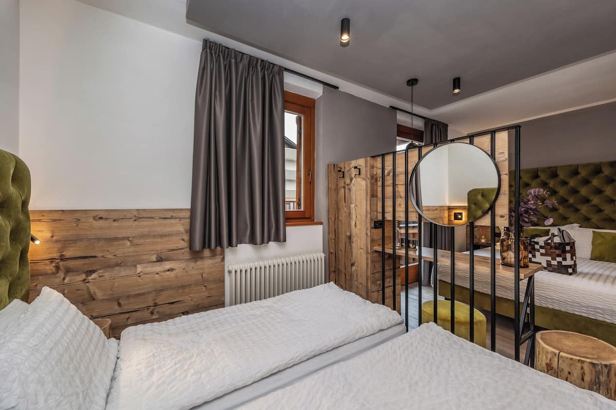 Ein modernes Hotelzimmer mit zwei Betten, einem Holz-Kopfteil, einem großen Spiegel und einem Fenster mit Vorhängen.
